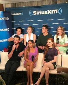 several people sitting on a white bench in front of a blue sign with the words siriusxm