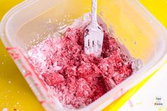 a plastic container filled with red powder and a fork in it's center, sitting on a yellow surface