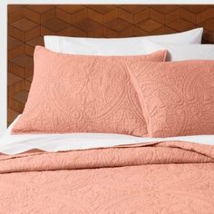 a bed with pink quilts and pillows on top of it, in front of a wooden headboard