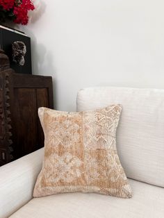 a white couch with a brown pillow on it's back and red flowers in the background