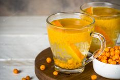 two mugs filled with orange juice and some chickpeas on a wooden tray