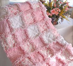 a pink and white crocheted blanket sitting on top of a table next to a vase with flowers