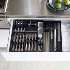 an open drawer with utensils and silverware in it next to a sink