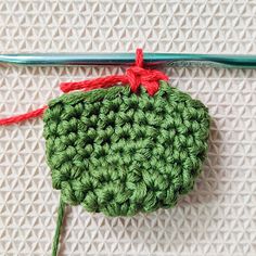 a crocheted green object with red string attached to it