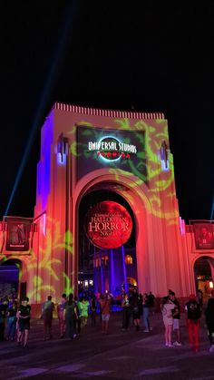 the entrance to universal studios at night with people standing in front and onlookers