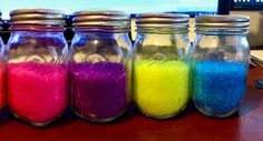 six jars filled with different colored sand on top of a wooden table in front of a computer screen