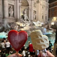 two heart shaped lollipops being held in front of a fountain