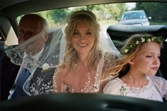 a bride and her flower girl are in the back seat of a car with their father