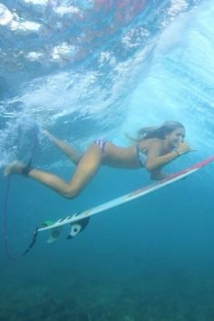 a woman is swimming in the ocean with her surfboard and holding on to a rope