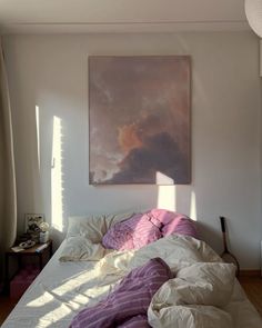 an unmade bed with purple and white comforter on it in front of a painting