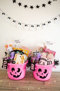 two pink buckets filled with candy and candies on top of a wooden table