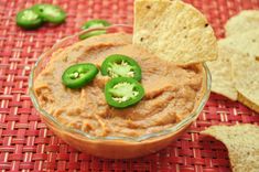 a bowl filled with guacamole and topped with green peppers next to tortilla chips