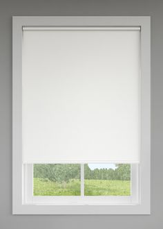 a window with white roller shades in front of a green field and trees behind it