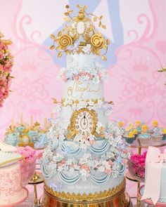 a three tiered blue and gold cake on a table with other desserts in the background