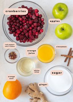 ingredients to make cranberry apple cider recipe displayed on white surface with oranges, ginger, cinnamon sticks and apples