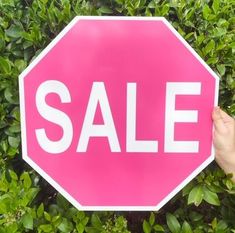 a person holding up a pink stop sign with the word sale written in white on it