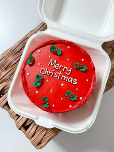 a merry christmas cake sitting in a plastic container on a wicker tray with the lid open