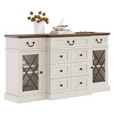 a white kitchen island with drawers and cupboards on top of it, next to a vase filled with flowers