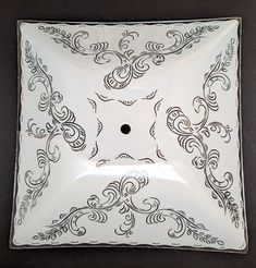 a white and black square plate with an intricate design on the center, in front of a dark background