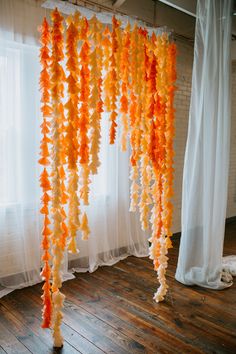 orange and white streamers hanging from the ceiling in front of a window with sheer curtains