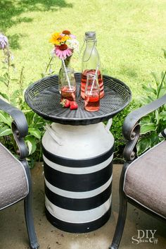 two chairs and a table with drinks on it in the grass next to some flowers