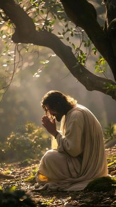 a man sitting on the ground praying under a tree