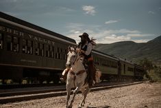 a man riding on the back of a white horse next to a train