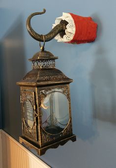 an old fashioned lantern hanging on the wall with a red cloth draped over it's top