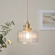 a glass light hanging from the ceiling next to a vase with flowers in it on a table