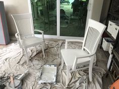 three white chairs sitting on top of a sheeted floor next to a large window