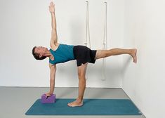 a man doing a yoga pose on a blue mat in front of a white wall