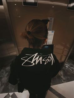 a woman standing in front of a mirror wearing a black jacket with white writing on it