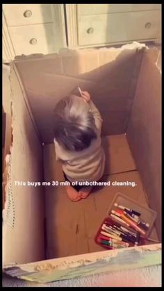 a little boy that is sitting in a box with some crayons on the floor