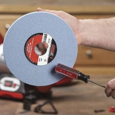 a hand holding a grinding disc with a red tool in it's left hand