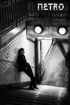 a woman sitting on top of a set of stairs in front of a metro sign