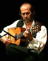 a man sitting down playing an acoustic guitar