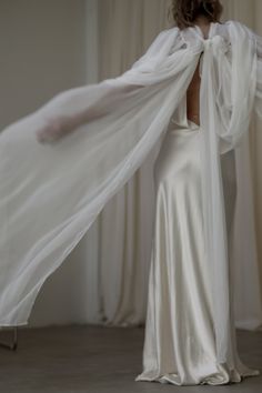 the back of a woman's dress with white fabric draped over her shoulders and arms