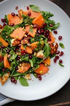 a white plate topped with carrots, spinach and pomegranate on top of a wooden table