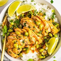 a white bowl filled with rice and chicken covered in sauce, garnished with lime wedges