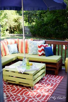 a patio with an umbrella, couch and table on the back deck in front of some trees