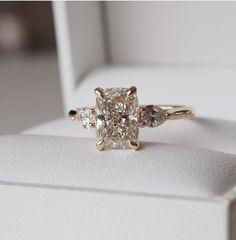 an engagement ring with three stones in it sitting on a white display box, close up