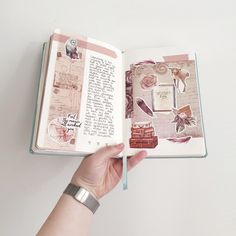 a hand holding an open book with pictures and writing on it's pages, in front of a white wall