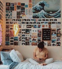 a woman sitting on top of a bed in front of a wall covered with pictures