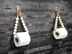 two rolls of toilet paper are hanging on the wall next to some wood bead necklaces