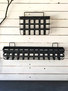 two black metal shelfs mounted to the side of a white wooden wall next to a tree