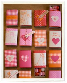 many small boxes with hearts and tags on them sitting on a wooden table next to some candies