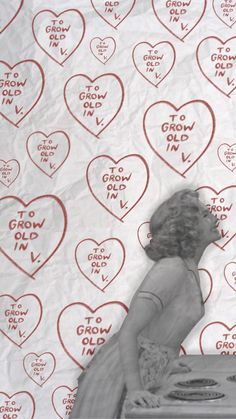 a woman sitting on top of a table next to a wall with hearts drawn on it