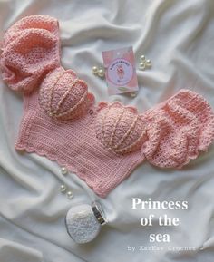 a pink knitted hat and diaper on top of a white sheet with pearls