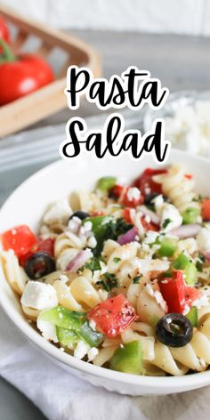 pasta salad in a white bowl with tomatoes, olives and feta cheese on the side