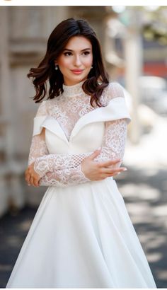 a woman in a white dress posing for the camera with her arms crossed and hands on her hips